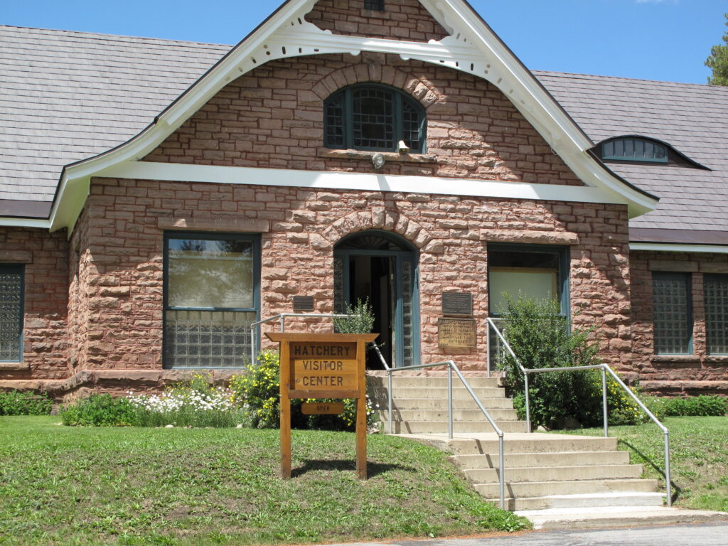 A reddish brick building with a small wooden sign along a staircase that says Hatchery Visitor Center